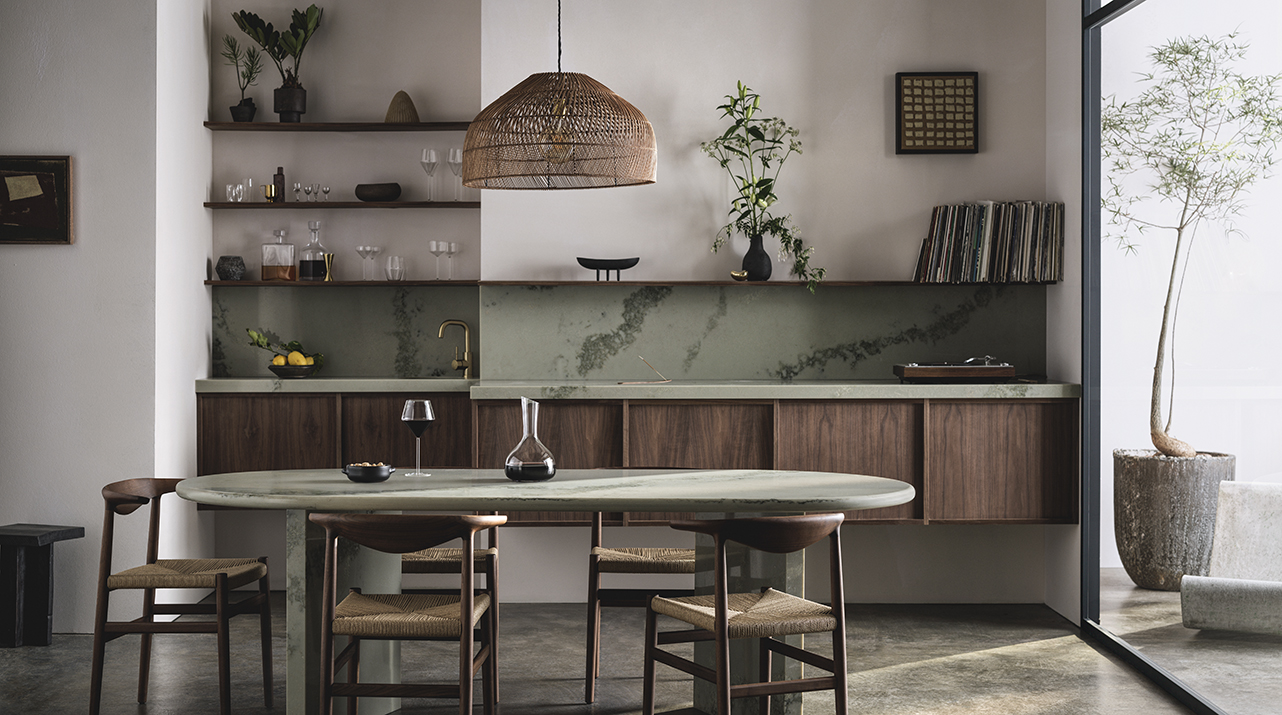Minimalist dining area with wooden table, chairs, pendant light, open shelves, plants, and large window.